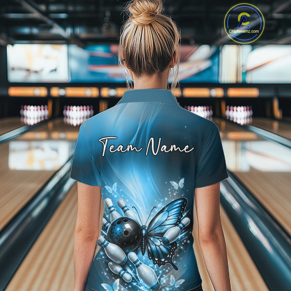 Back view of a female model in a bowling center wearing a blue quarter-zip shirt featuring a butterfly beside a bowling ball and pins.