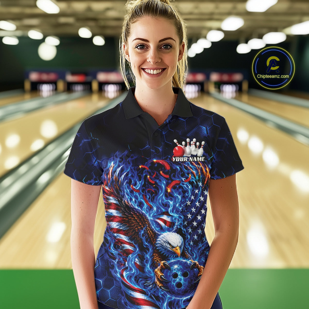 Female model front view in a bowling lane wearing a polo shirt with flaming bald eagle artwork, blue bowling ball, American flag, and blue flames.