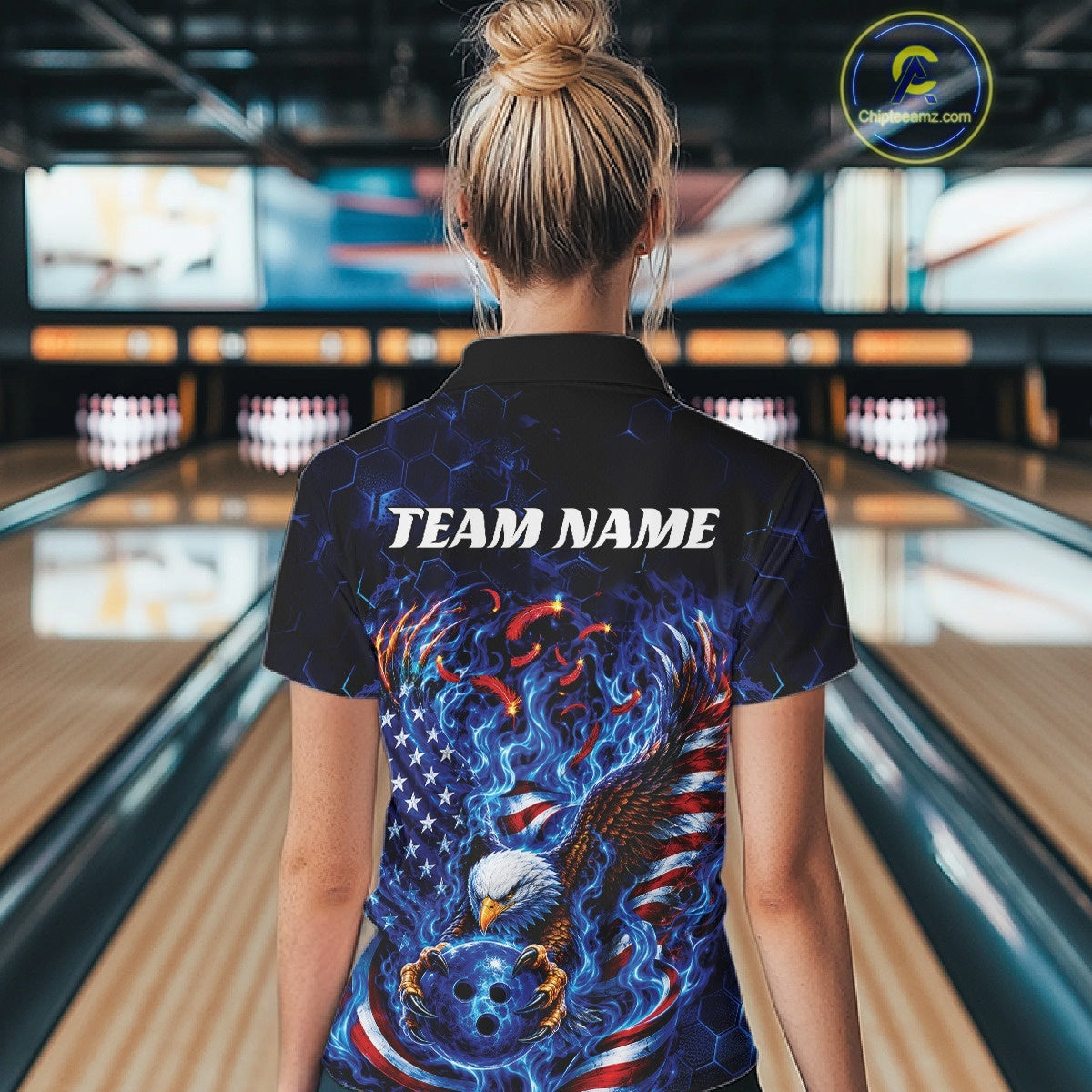 Back view of a female model at the bowling lane wearing a polo shirt with flaming bald eagle, blue bowling ball, American flag, and blue flames.
