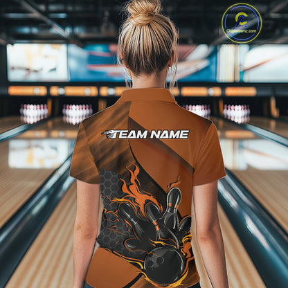 Female model at a bowling lane, back view of black and orange quarter zip shirt showcasing flame bowling ball striking pins with hexagon accents