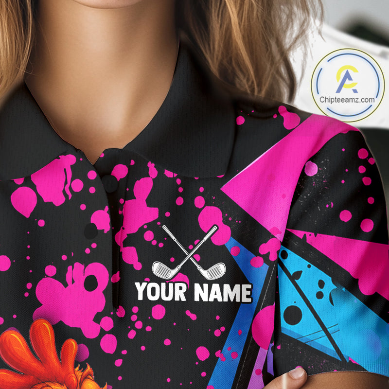 A close-up of a person wearing a black polo shirt with a vibrant custom print. The design features hot pink paint splatters, a bright blue geometric pattern on the sleeve, and a white customizable text placeholder reading 'YOUR NAME' with crossed golf clubs above it.