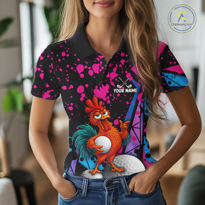 A woman wearing a short-sleeve polo shirt with a colorful graphic print featuring a cartoon rooster, golf balls, and pink paint splatters on a black background. The shirt has a custom placeholder design with the text 'YOUR NAME' and a golf club icon.