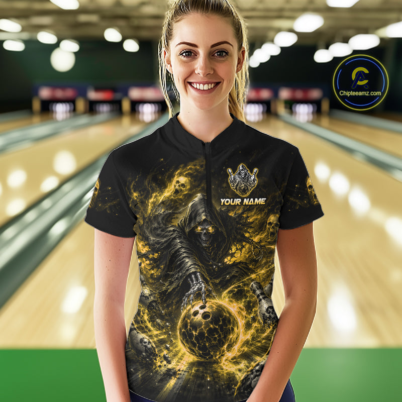 Woman wearing a black and yellow shirt with a design of a skeleton holding a bowling ball in a bowling alley.