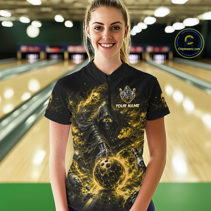 Woman wearing a black and yellow shirt with a design of a skeleton holding a bowling ball in a bowling alley.