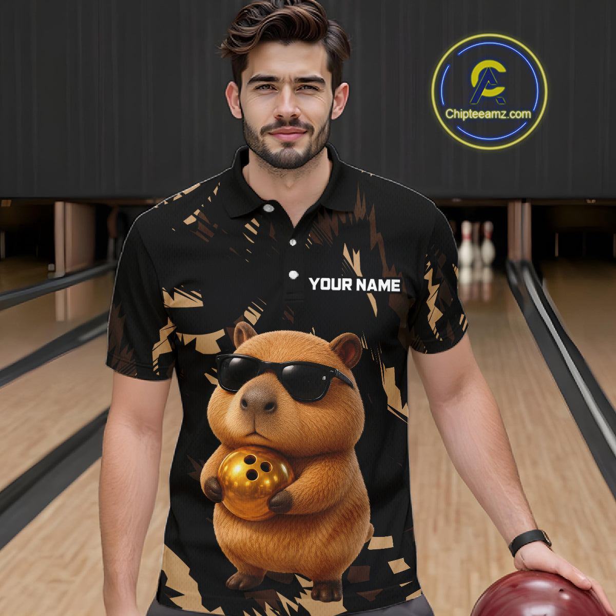 Man wearing a black shirt with a capybara holding a bowling ball design in a bowling alley.