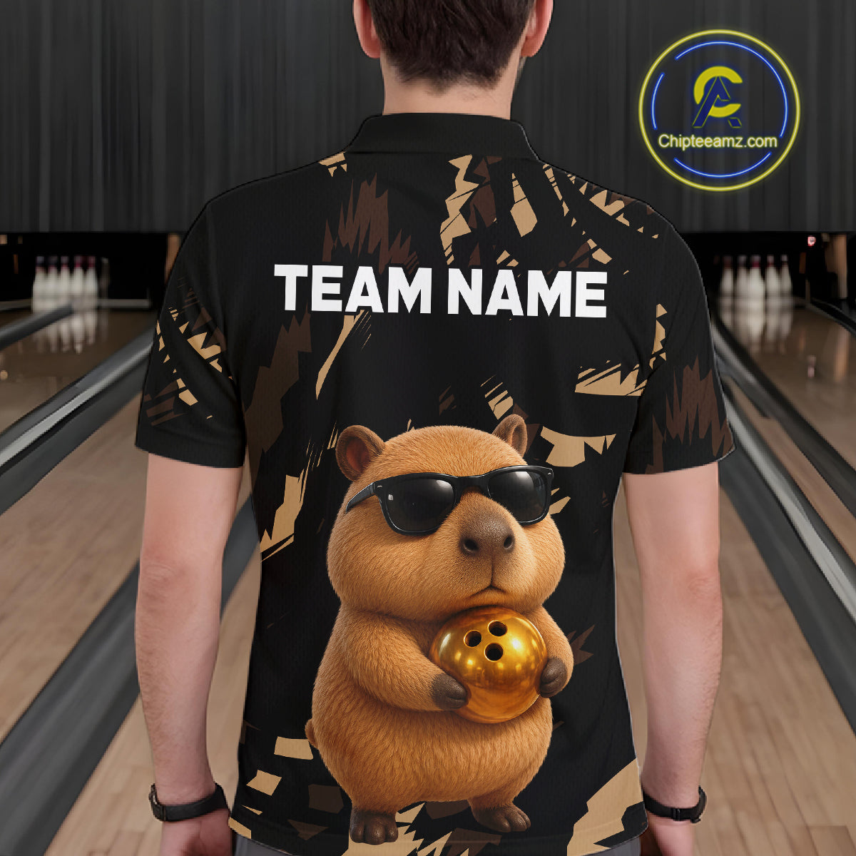 Person wearing a black shirt with a capybara graphic holding a bowling ball in a bowling alley.