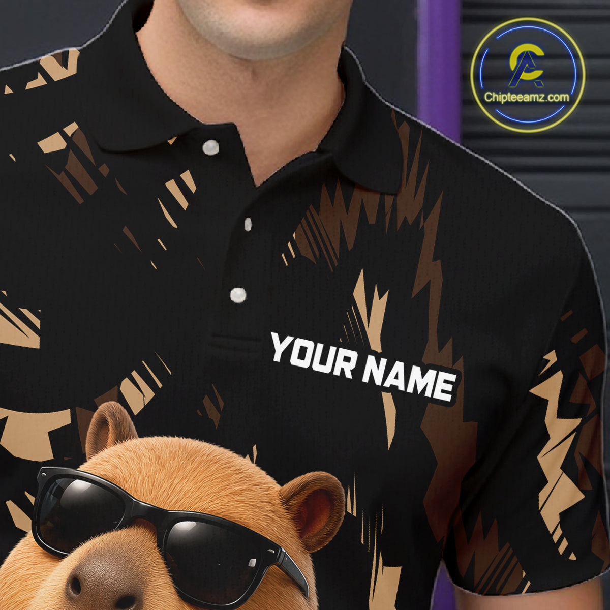 Black polo shirt with gold abstract design and 'Your Name' text, worn by a person, with a capybara wearing sunglasses in the foreground.