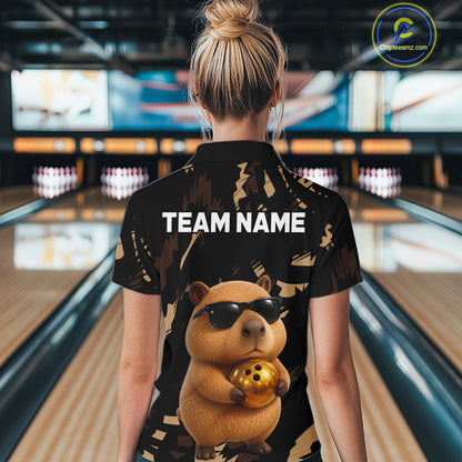 Person wearing a black shirt with a capybara graphic and 'TEAM NAME' text in a bowling alley.