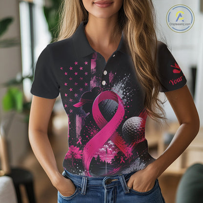 A woman wearing a black short-sleeve polo shirt with a pink and black graphic print featuring a ribbon, golf ball, and stars, paired with blue jeans in a blurred indoor setting.