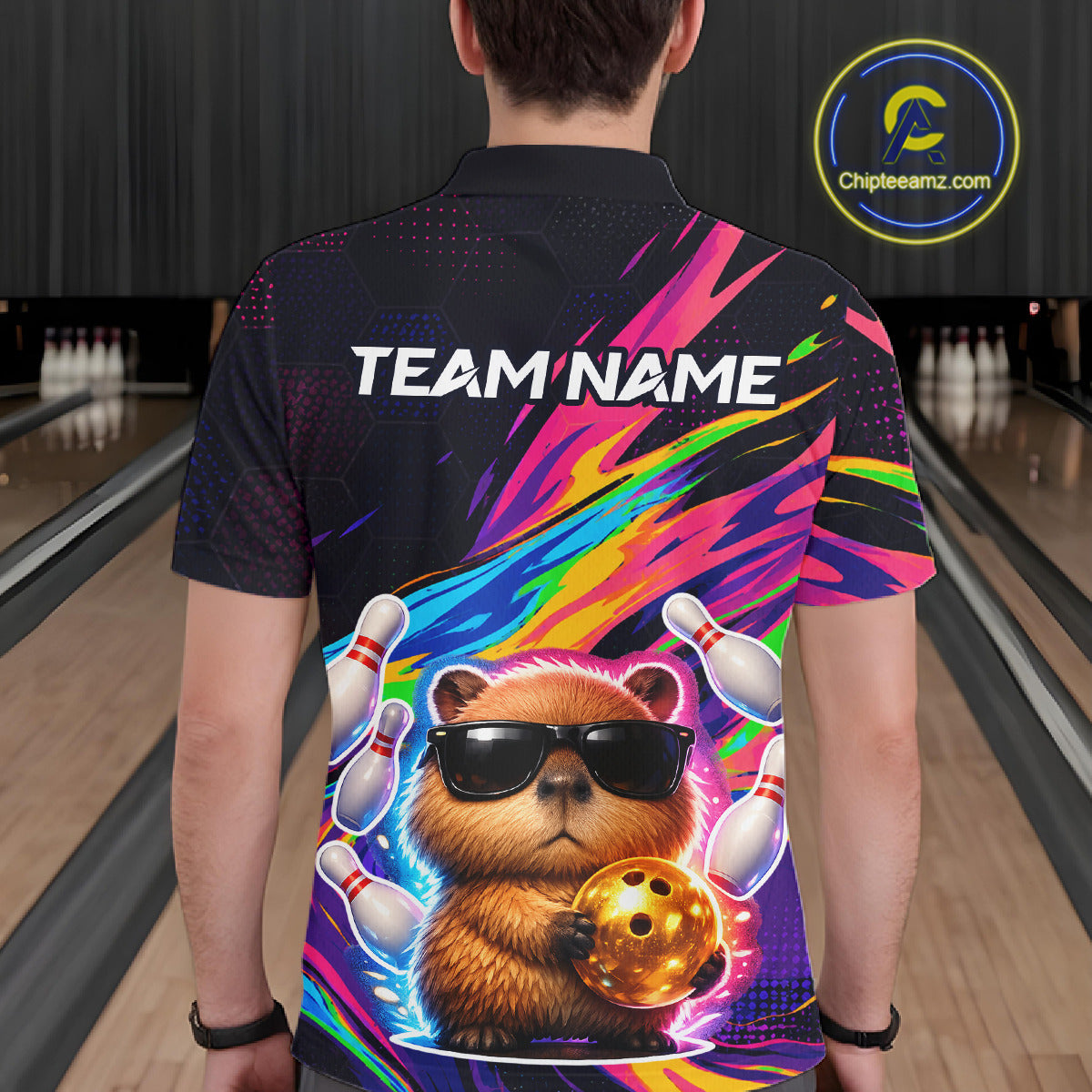 Person wearing a colorful bowling shirt with a capybara holding a bowling ball and text 'TEAM NAME' in a bowling alley.