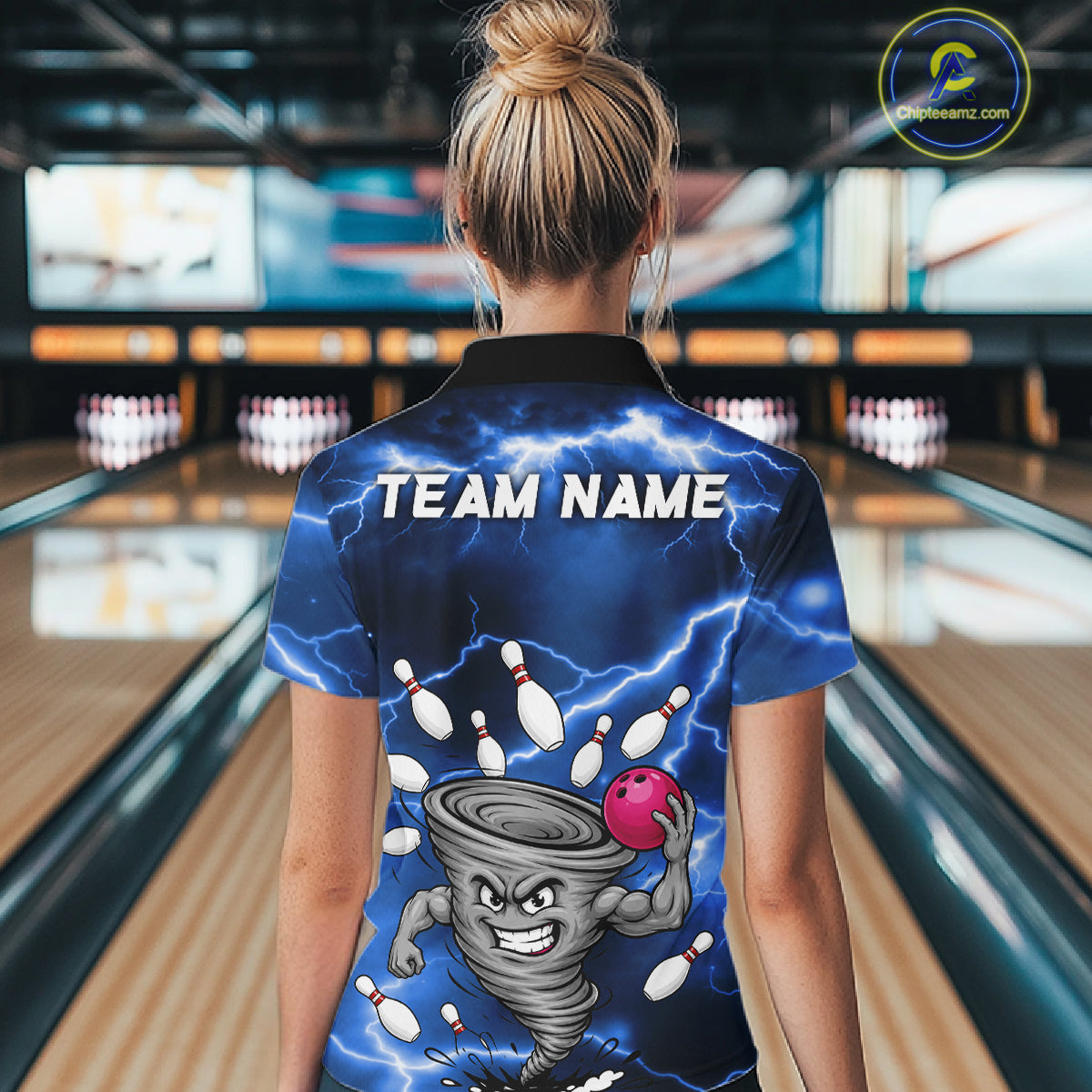 Back view of woman wearing a blue thunder lightning tornado bowling polo shirt inside a bowling alley.