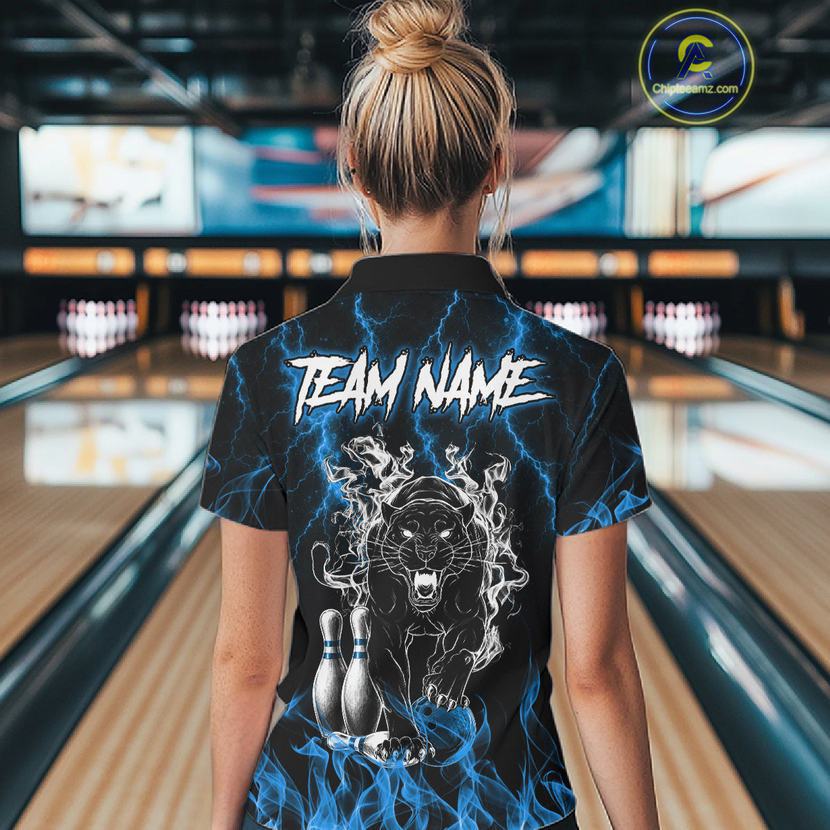 Back view of woman wearing a blue flaming panther bowling polo shirt inside a bowling alley.