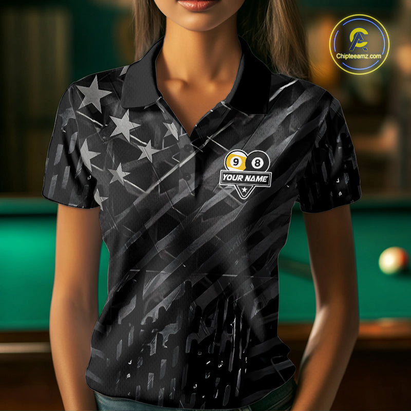 Woman wearing a black polo shirt with pool ball design and text, holding a pool cue in a billiards setting.