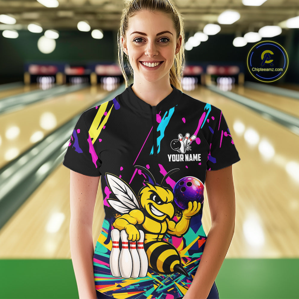 Person wearing a black bowling shirt with colorful design and bee graphic in a bowling alley.